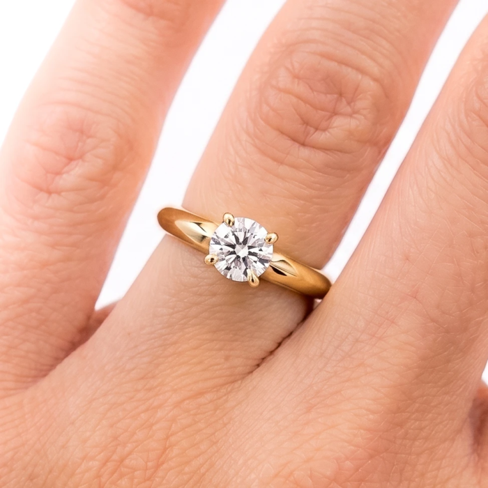 Anillo de compromiso oro 18K con un diamante talla brillante central en la mano de la modelo